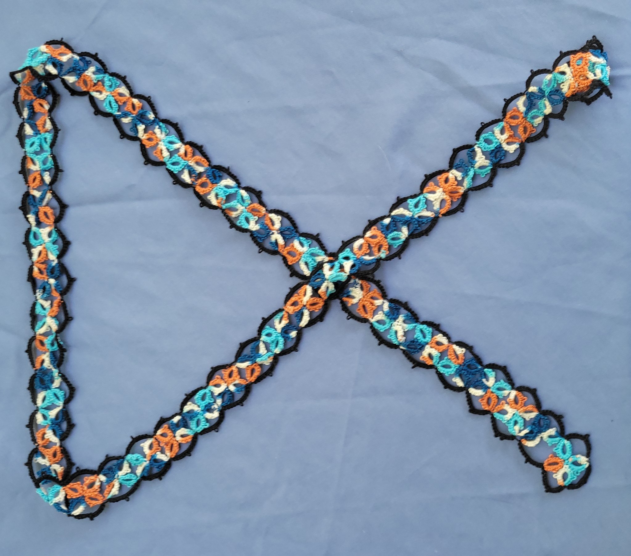 Hand-tatted lace scarf featuring colorful turquoise, aqua, navy, orange, cream, and black motifs arranged in a repeating pattern.