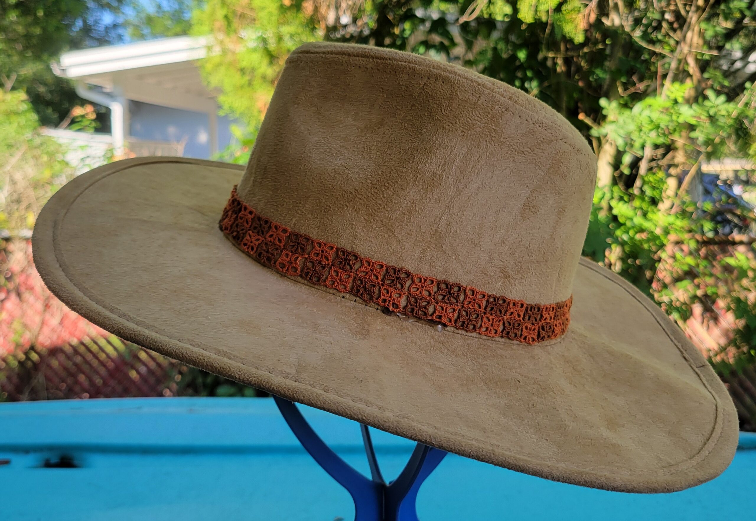 Rust-orange hand-tatted lace hat band displayed around a neutral-colored wide-brim hat outdoors