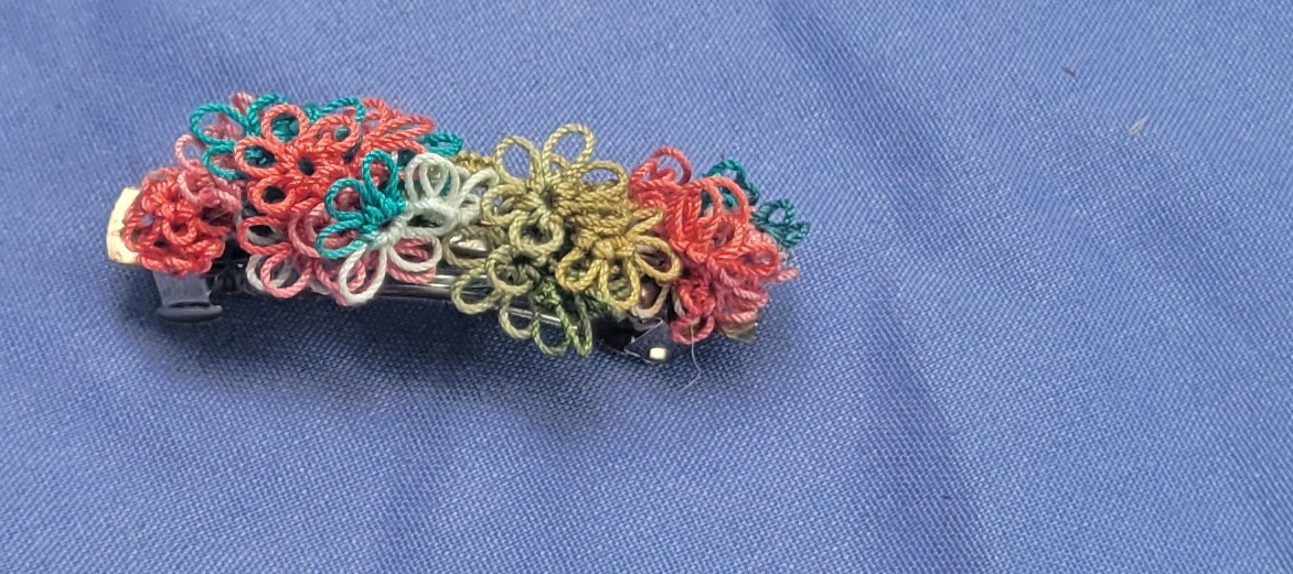 Colorful hand-tatted lace barrette with coral, turquoise, teal, white, and golden olive floral motifs, approximately 1.75 inches long.