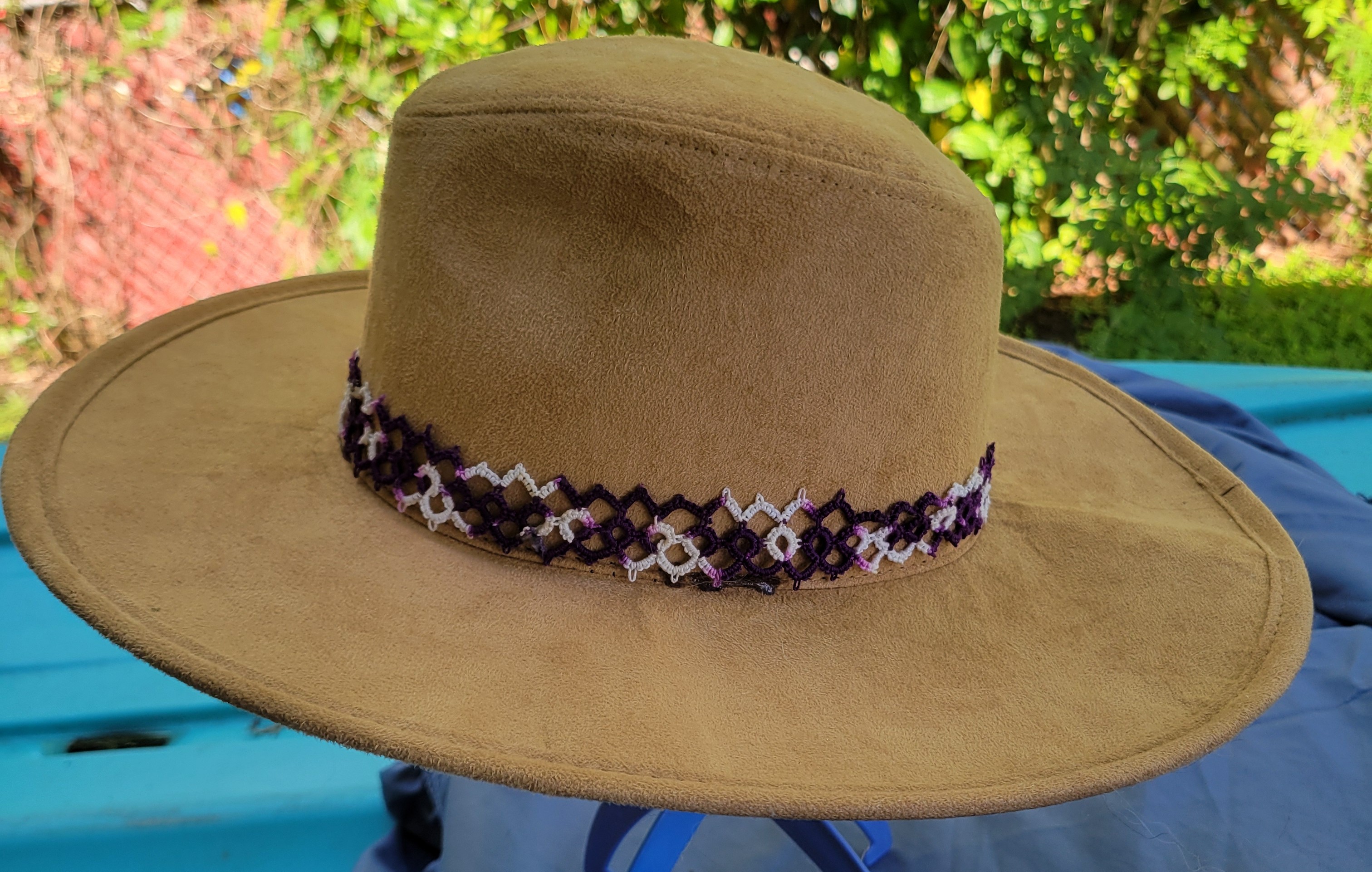 Purple and white hand-tatted lace hat band displayed on a tan hat